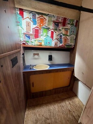 A compact bathroom with a sink, wooden cabinetry, and a colorful wall decoration above the mirror. - Rustic Boat Glamping Retreat with Mountain Views near Rio Peñasco in Mayhill, New Mexico (Mayhill)