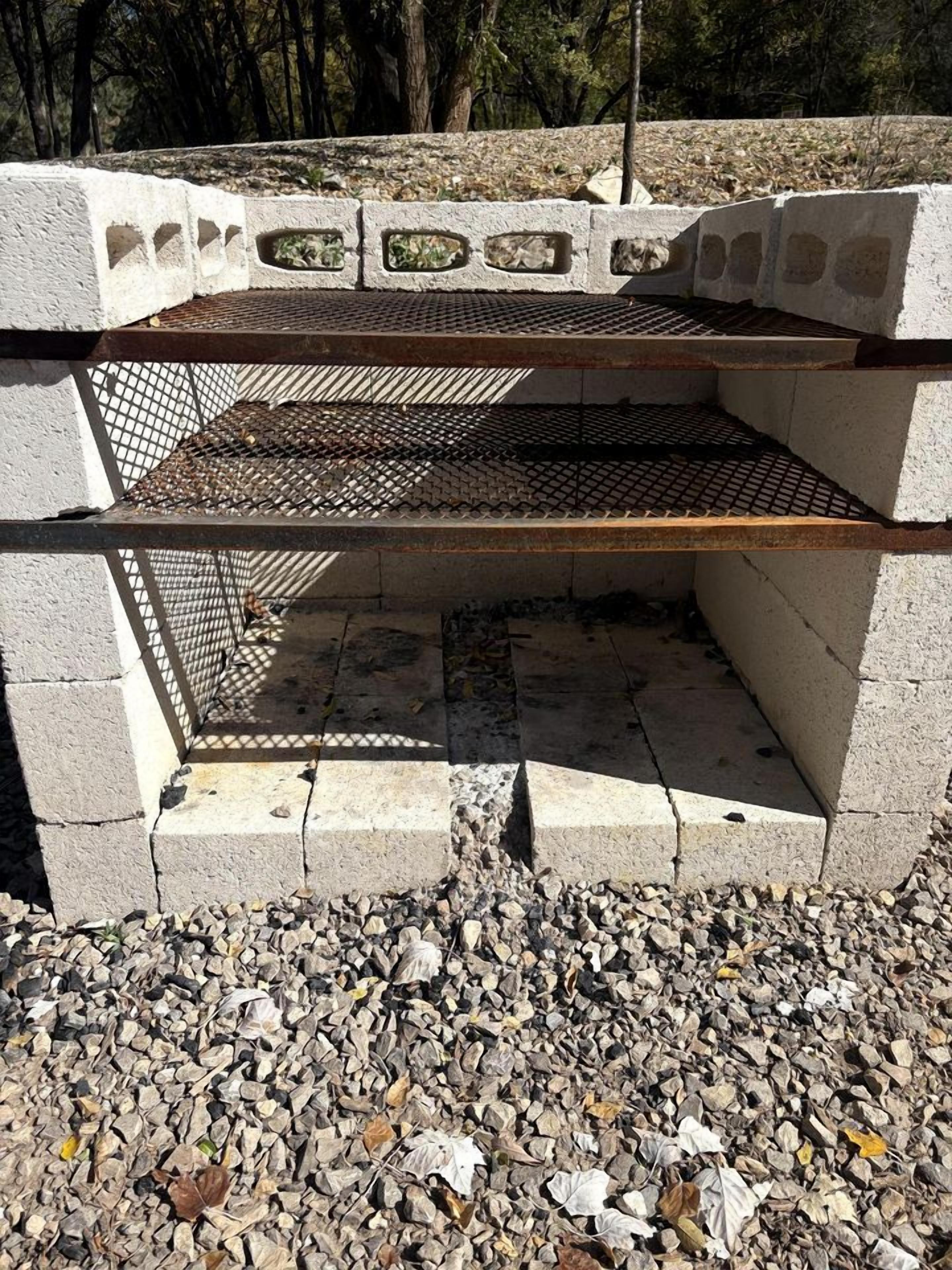 A concrete structure with a metal grill, surrounded by gravel and trees.