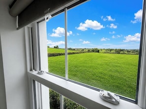 Ein Fenster mit Blick auf ein grünes Feld und einen strahlend blauen Himmel.