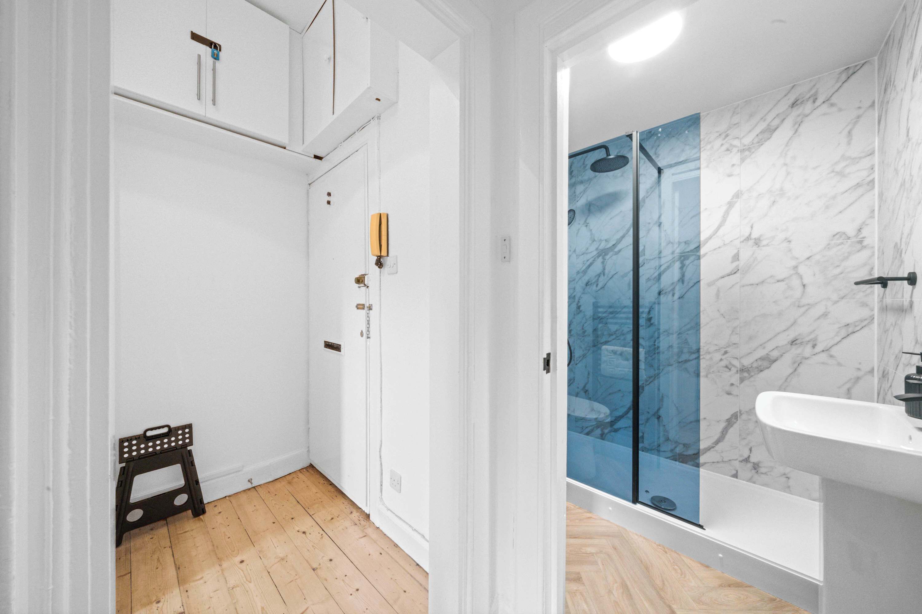 A modern bathroom with a glass shower enclosure, a white sink, and wooden flooring.