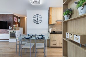 A modern kitchen with a clock, wooden cabinets, and a dining area with a glass table and chairs. - Apartment 'T2 Reis' with Shared Pool, Wi-Fi, and Air Conditioning (Albufeira)