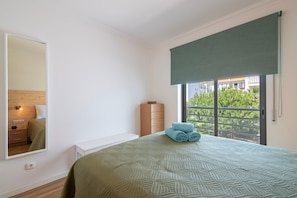 A bedroom with a bed, a dresser, a mirror, and a window with a view. - Apartment 'T2 Reis' with Shared Pool, Wi-Fi, and Air Conditioning (Albufeira)