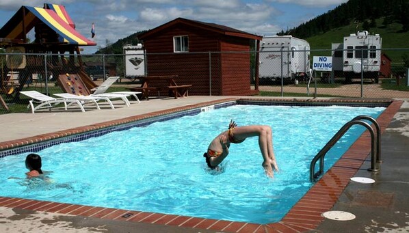 A swimming pool with a diving board, lounge chairs, and a small cabin in the background.