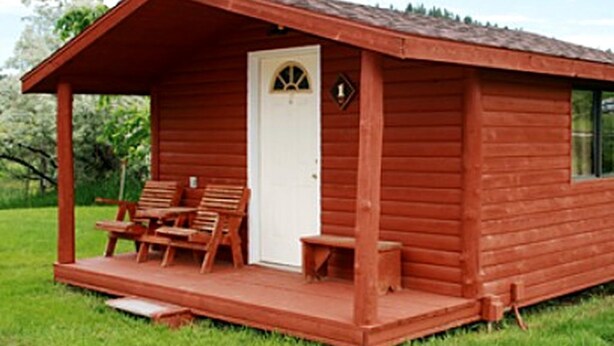Una pequeña cabaña de madera con un porche, una puerta y dos sillas de madera.
