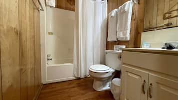 Een badkamer met houten lambrisering, voorzien van een badkuip, toilet en een wastafel met spiegel.