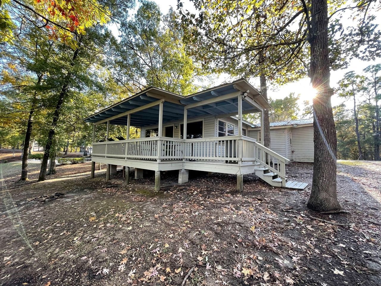 A covered porch with a staircase leading to a house, surrounded by trees and a leaf-covered ground.