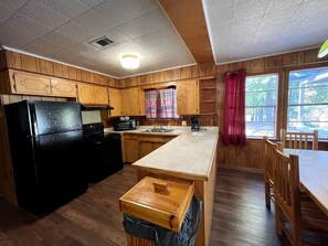 Eine Küche mit Holzausstattung, einem schwarzen Kühlschrank, einer Spüle und einem Essbereich mit Tisch und Stühlen.