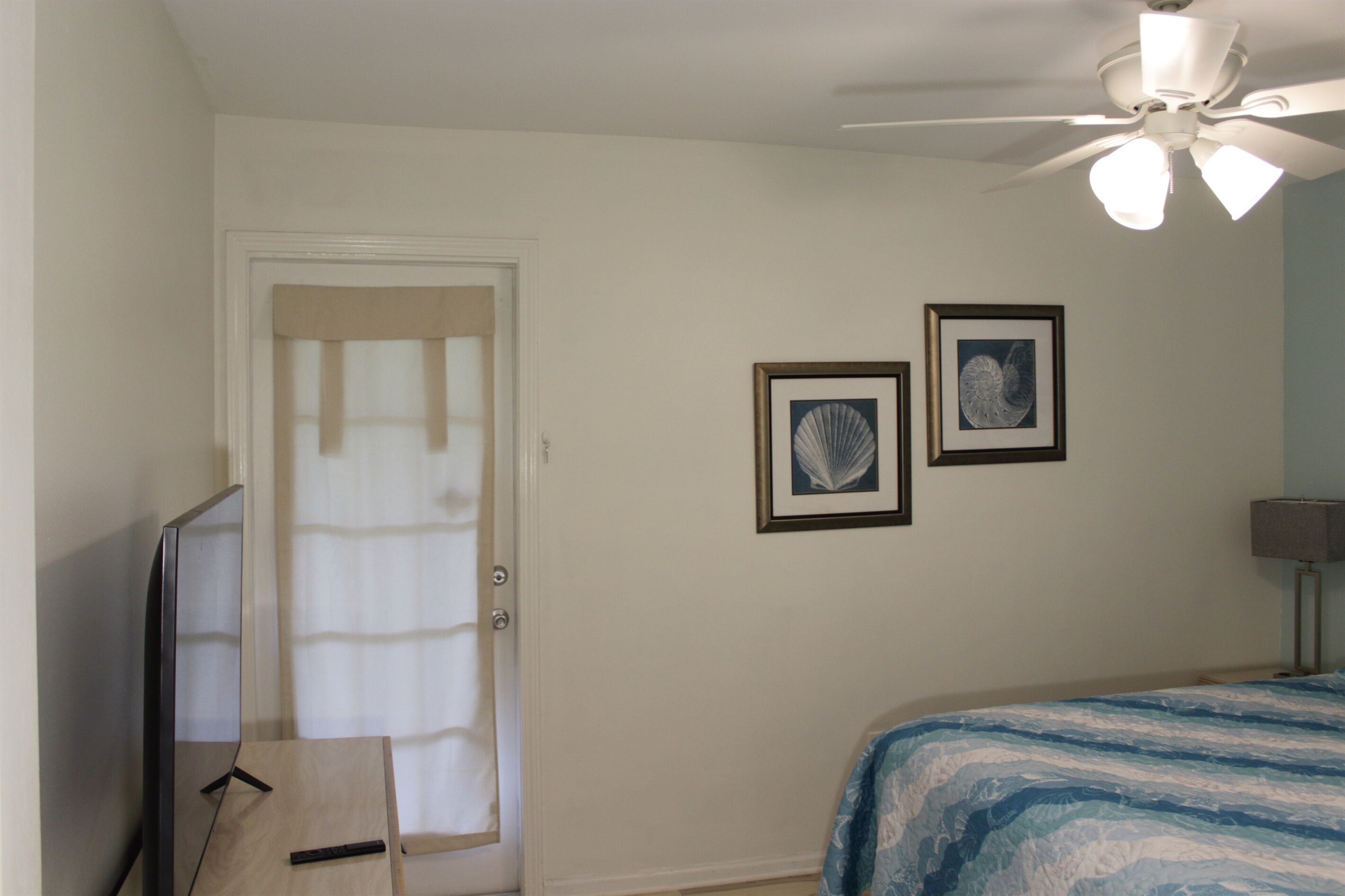 Une chambre à coucher avec un lit, un ventilateur de plafond, un téléviseur et deux tableaux encadrés accrochés au mur.