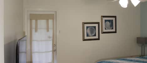 A bedroom with a bed, a ceiling fan, a television, and two framed pictures on the wall.