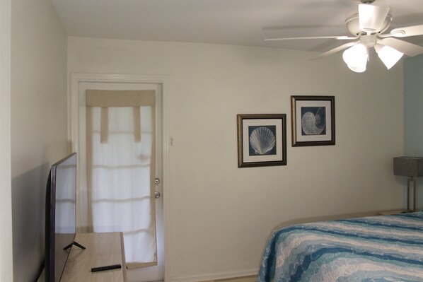 A bedroom with a bed, a ceiling fan, a television, and two framed pictures on the wall.