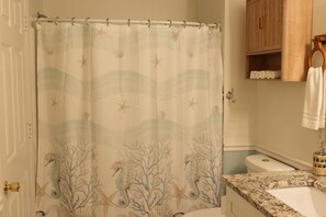 Un baño con cortina de ducha de diseño marino, un mueble de madera y encimera de mármol.