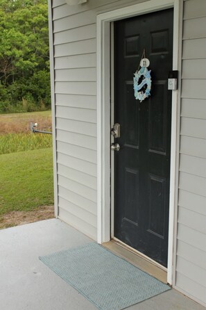 A black door with a welcome wreath, a doorbell, and a doormat.