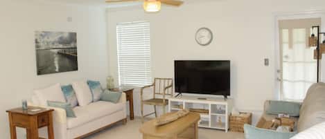 A living room with a sofa, a coffee table, a television, and a ceiling fan.