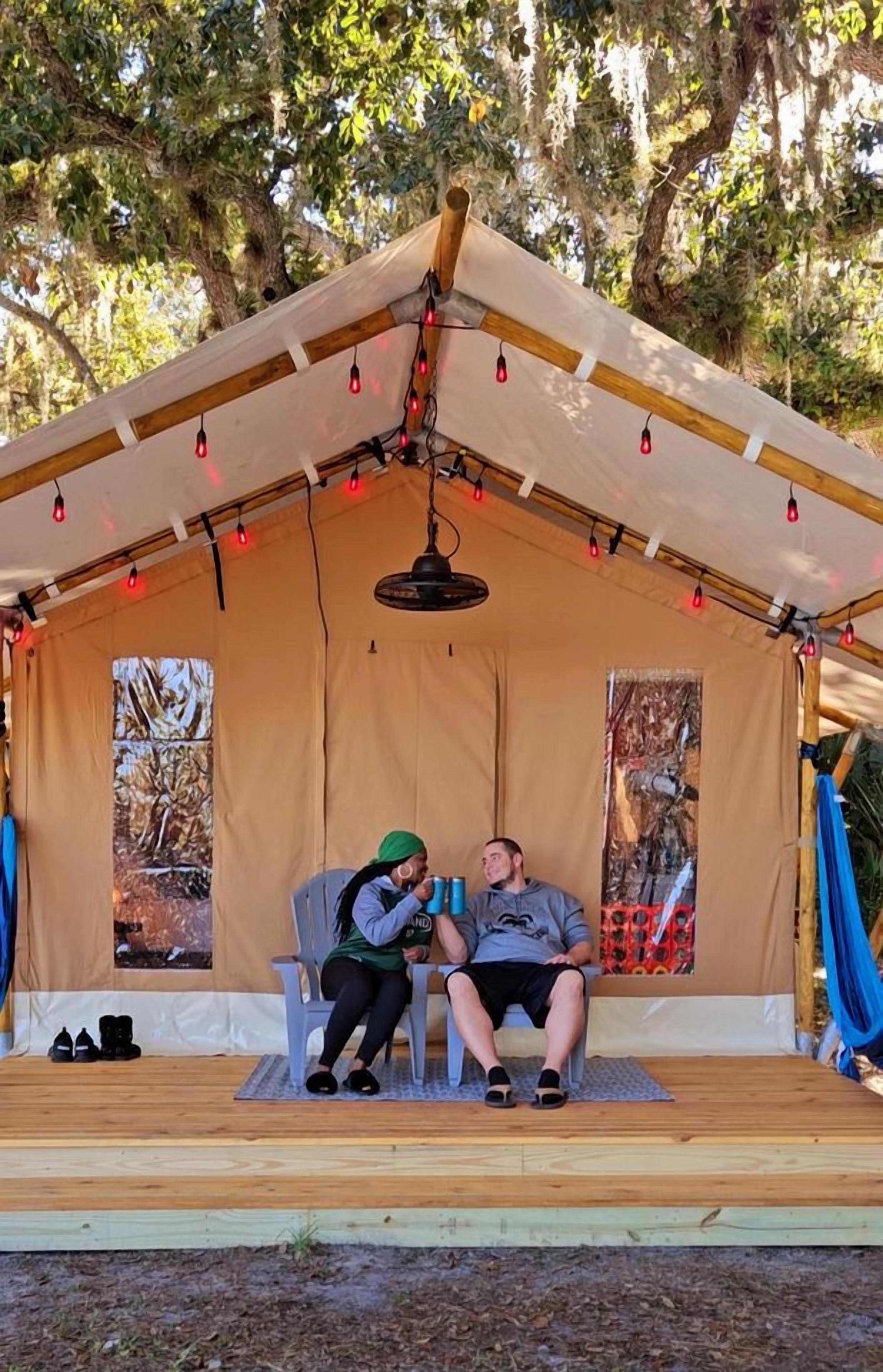 A tent with two chairs, a hanging light fixture, and a wooden deck.