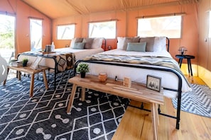 A tent-style room with two beds, a wooden table, and a patterned rug.