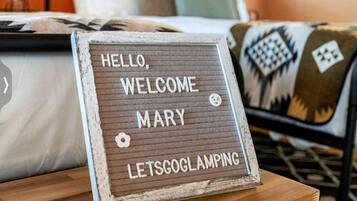 Uma cama com um letreiro que diz 'HELLO, WELCOME MARY LETSGOGLAMPING' em cima de uma mesa de madeira.
