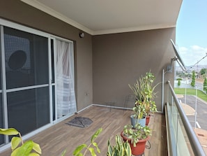 A balcony with a sliding glass door, potted plants, a metal railing, and a view of the street. - Cozy 1-bedroom apartment with a pool, standby genset in tranquil West Hills (Accra)