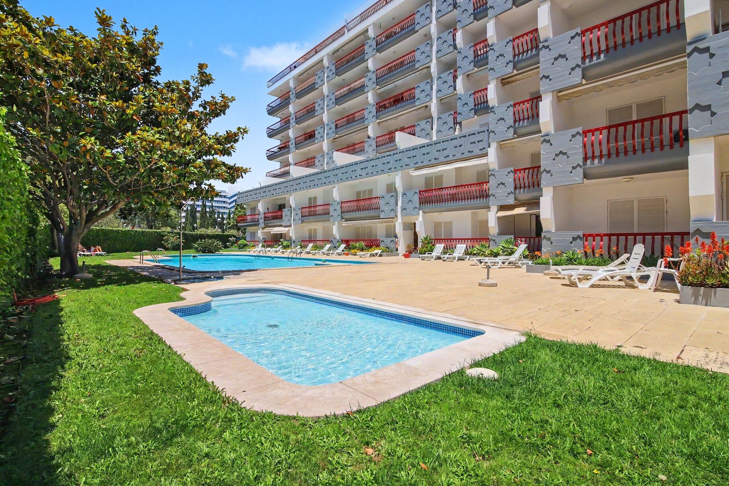 A hotel with a swimming pool, outdoor lounge chairs, and a well-maintained garden.