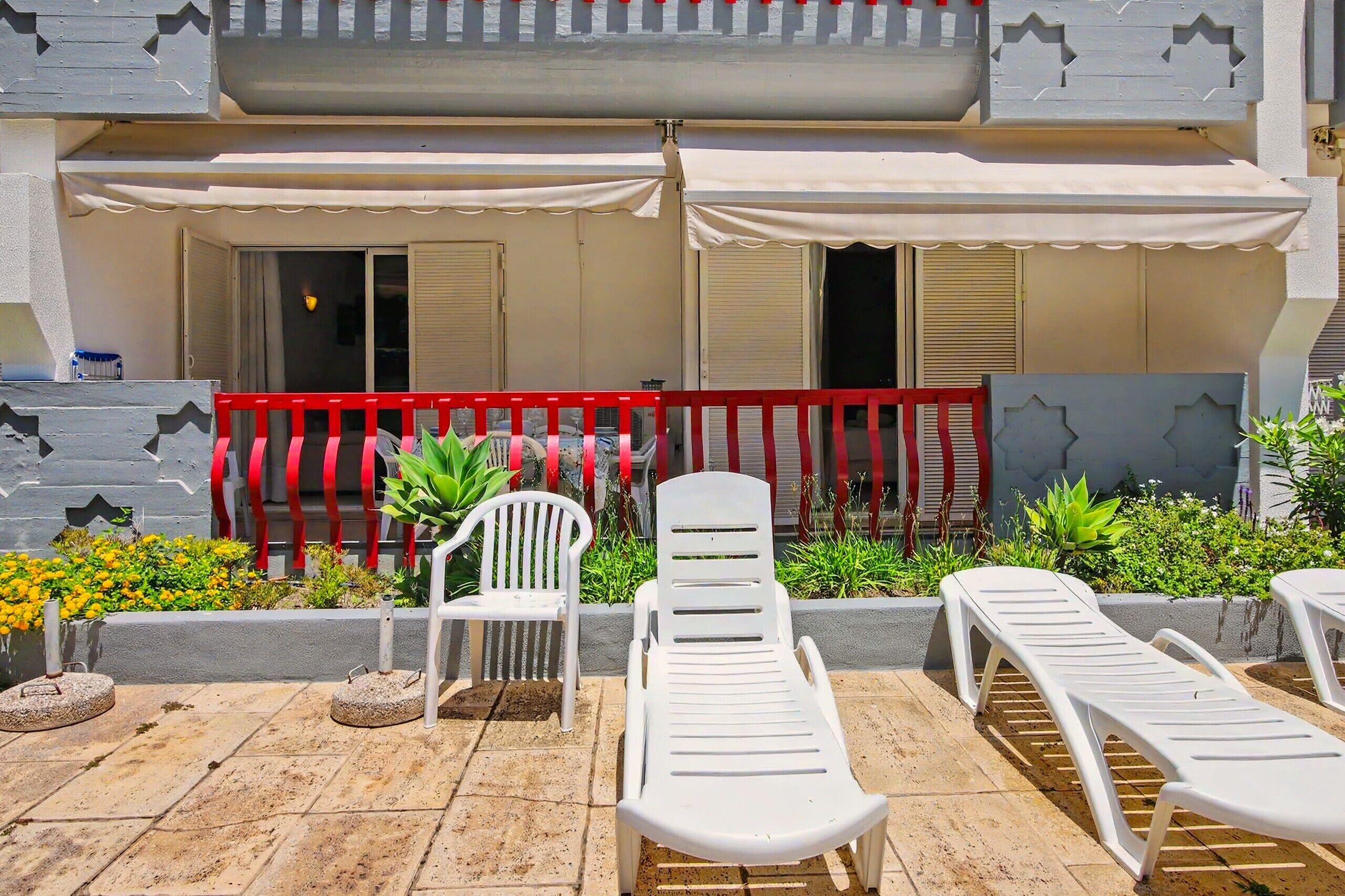 A terrace with white lounge chairs, a red and white striped fence, and potted plants.
