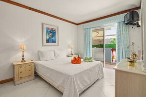 Ein Schlafzimmer mit einem Bett, Nachttischen, einer Kommode, einem Fernseher und einem Fenster mit Vorhängen.