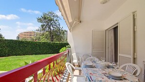 Een balkon met een rode reling, een tafel gedekt met borden en glazen, en uitzicht op een gebouw en groen.
