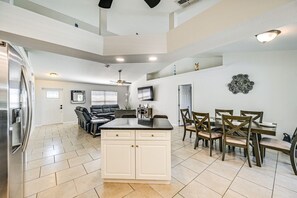 A spacious kitchen with a central island, dining area with wooden chairs, and a living room with a sofa and TV. - Spacious 4-BR with Patio, Dock + Canal Access (Cape Coral)