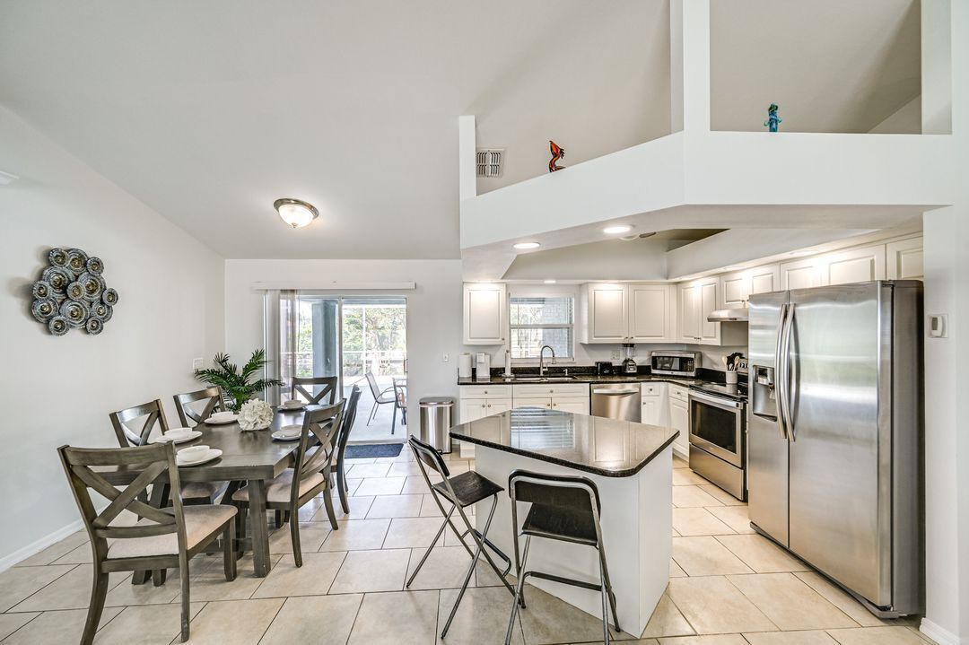 A modern kitchen with white cabinets, a stainless steel refrigerator, and a dining area with a table and chairs.
