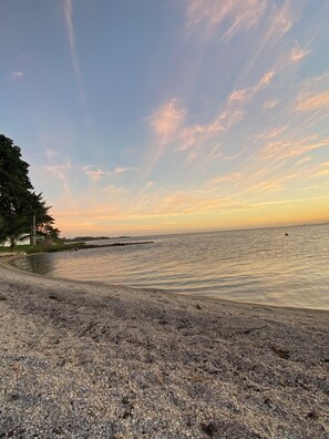 A beach with pebbly shore, calm water, and a clear sky. - Beach Studio Apartment (São Pedro da Aldeia)