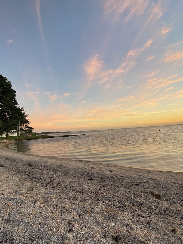 A beach with pebbly shore, calm water, and a clear sky.