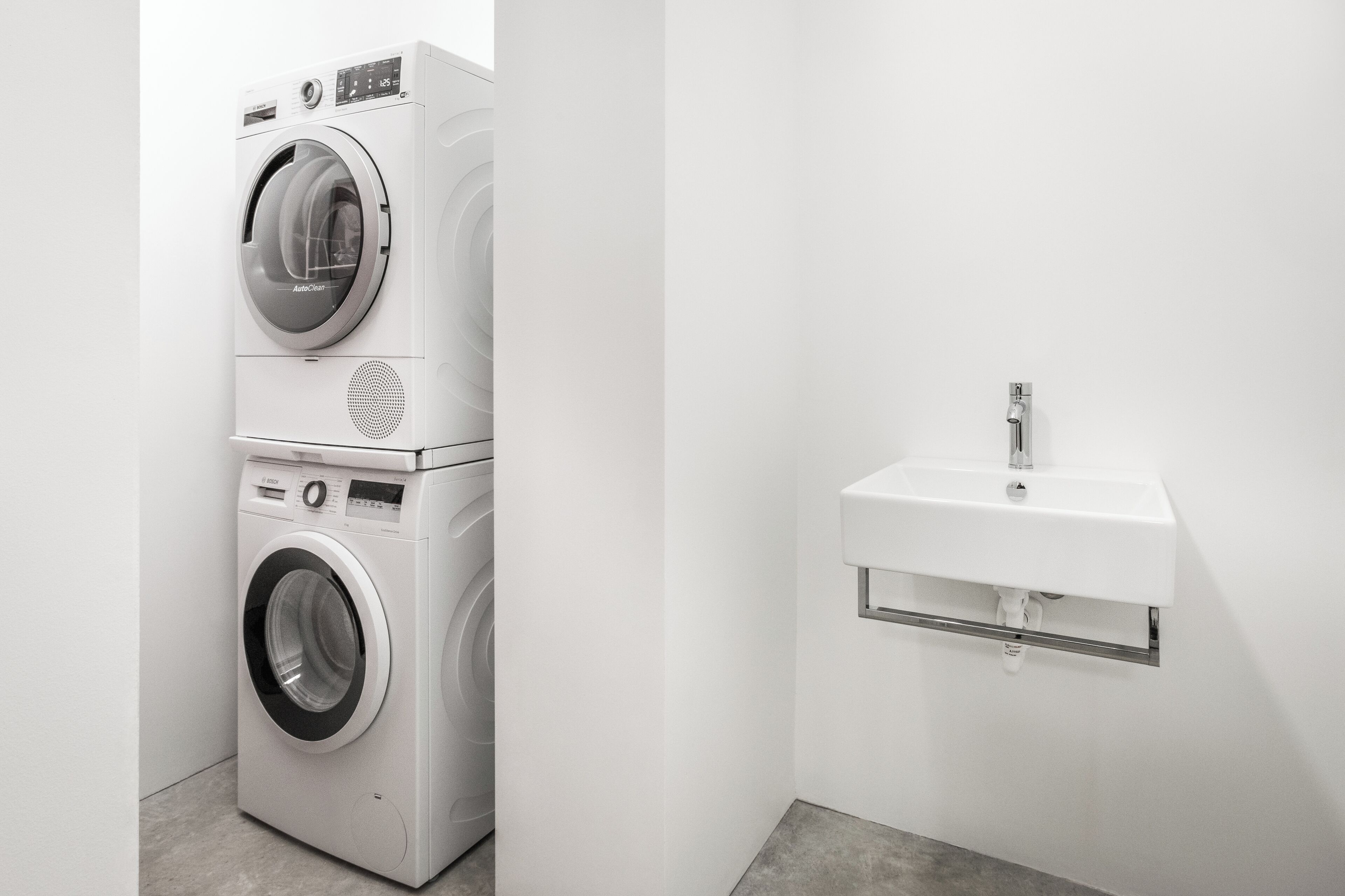 A modern laundry area with stacked washing machines and a built-in sink.