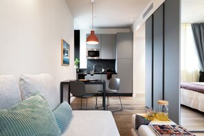 Una habitación de hotel moderna con sofá, una mesa de comedor con sillas, zona de cocina y cama.