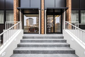 Entrada de un edificio con una escalera, una cámara de seguridad y un rascacielos al fondo.