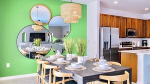 Een moderne keuken met houten kastjes, roestvrijstalen apparatuur en een eethoek met een groene wand en spiegels.