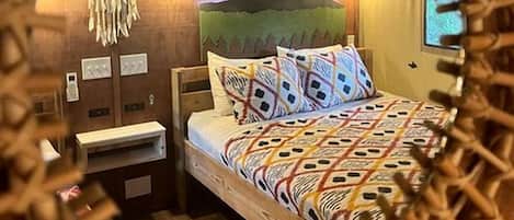Una stanza con un letto, un comodino, una lampada a muro e una testiera decorativa.