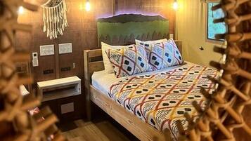 A room with a bed, bedside table, wall-mounted light, and a decorative headboard.