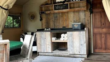 A rustic tent interior with a wooden bench, a sign reading 'Wright Lamp,' and a small table with a lamp.