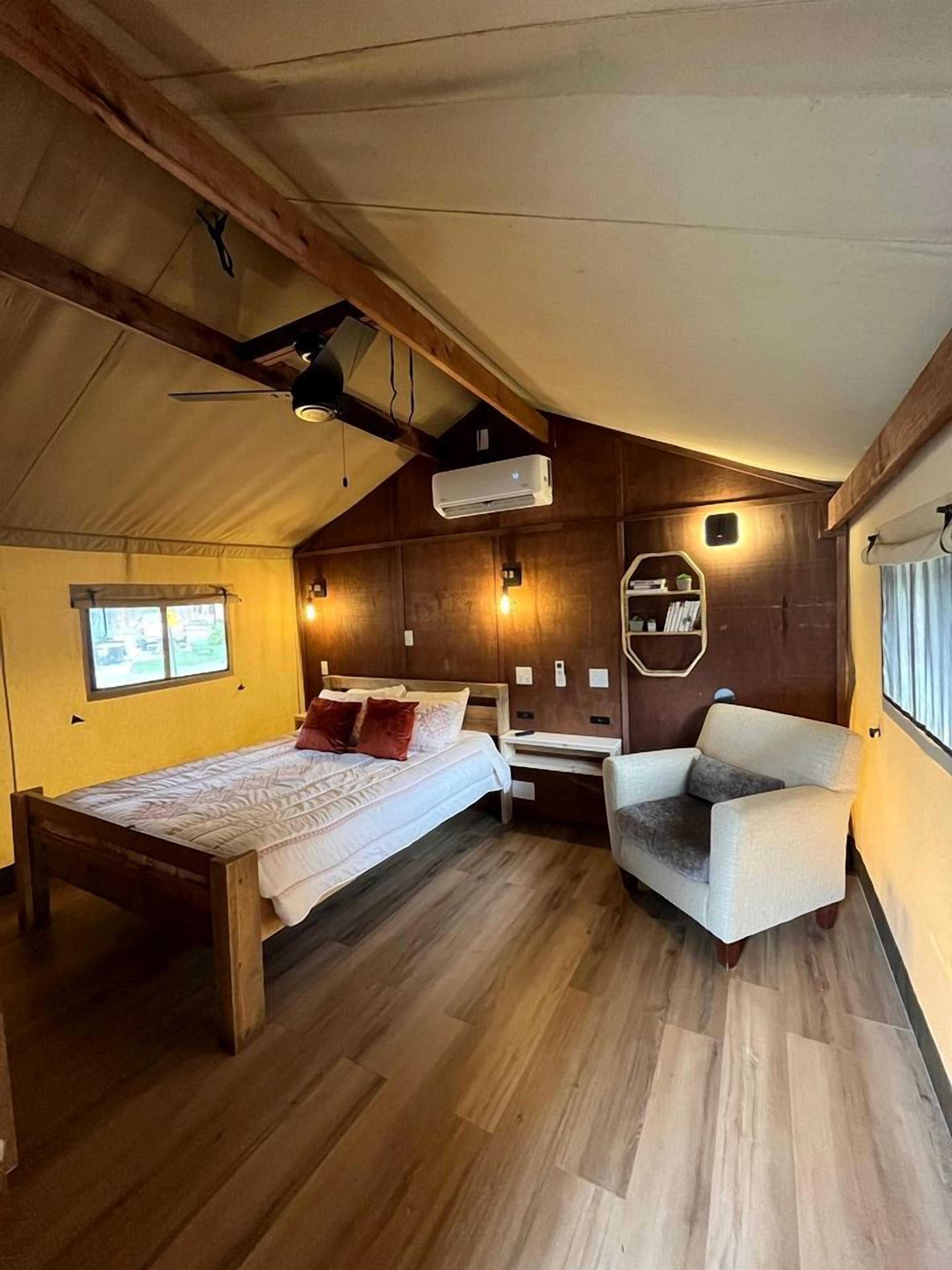 A tent-style room with a bed, a chair, a small table, and a window.