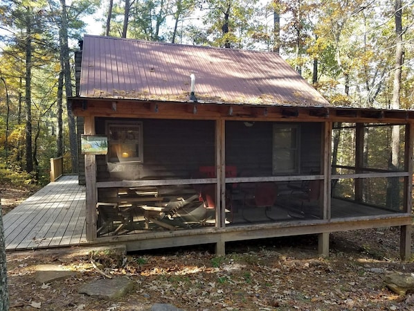 A cabin with a metal roof, a wooden deck, and a large window.