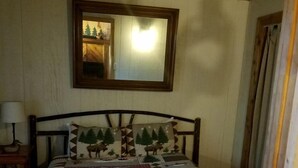A wooden-paneled room with a bed, a nightstand, a mirror, and a door.
