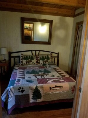 A wooden-paneled room with a bed, a nightstand, a mirror, and a door.
