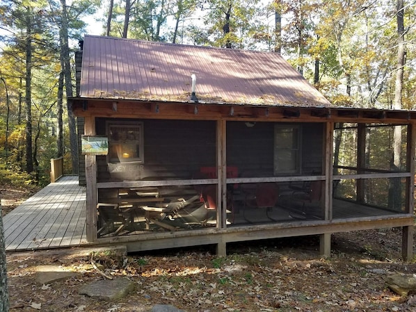 A cabin with a metal roof, a wooden deck, and a large window.