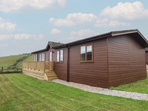 A two-story wooden building with a balcony, a gravel pathway, and a grassy field in the background. - Lodge 19 (Torpoint)