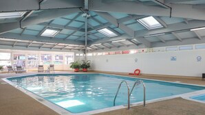 An indoor swimming pool with clear water, surrounded by lounge chairs and potted plants. - Lodge 19 (Torpoint)