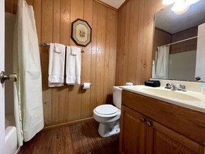 A wooden-paneled bathroom with a toilet, a sink, and a mirror. - Cozy Waterfront Cabin with Private Pond Views and Outdoor Deck Near Zwolle, Louisiana (Zwolle)