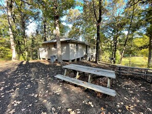 Eine Hütte mit Veranda, umgeben von Bäumen, mit einem Picknicktisch im Vordergrund.