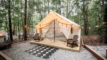 A tent with two chairs and a checkered mat in a forest.