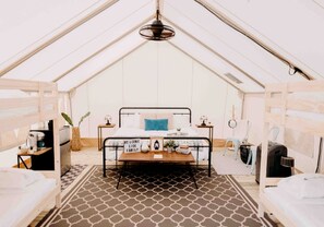 A tented accommodation with a central bed, bedside tables, a hanging light fixture, and a patterned floor.