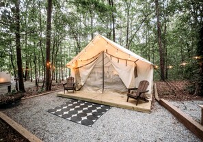 A tent with two chairs and a checkered mat in a forest.