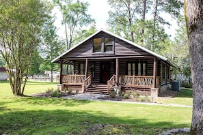 A log cabin with a porch, surrounded by trees and grass. - Fully Restored Cabin with Private Hut-Tub in Livingston, Texas (Livingston)