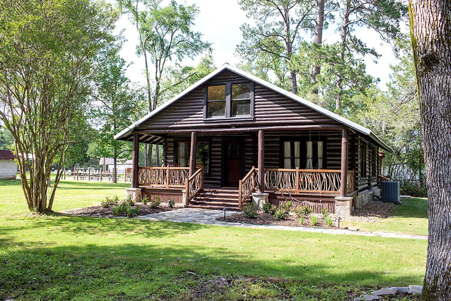 A log cabin with a porch, surrounded by trees and grass.